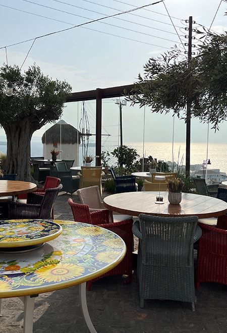 Outdoor dining area at Nusret Mykonos overlooking the Aegean Sea, featuring colorful Mediterranean-inspired tables and chairs.