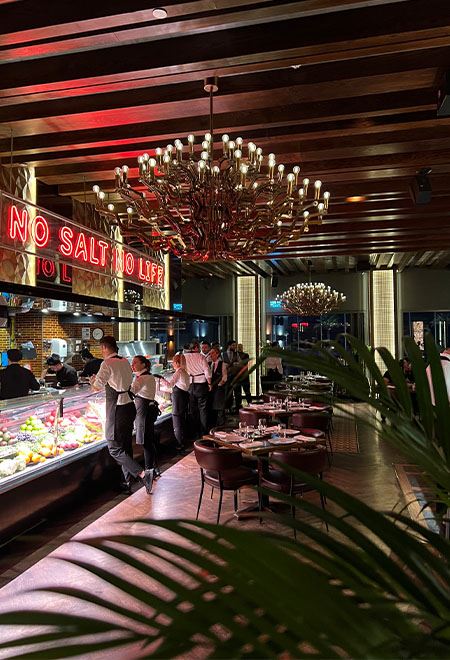 Luxurious dining at Nusr-Et Doha with a vibrant interior featuring chandeliers and a neon sign 'No Salt No Life,' creating an upscale steakhouse ambiance.