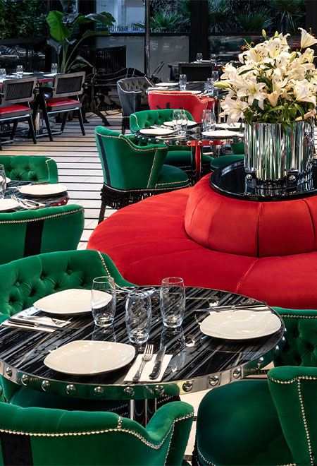 Stylish dining setup at Nusr-Et Etiler, featuring bold green and red velvet chairs, black marble tables, and a vibrant upscale ambiance.