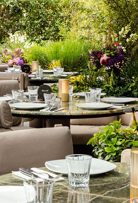 Beautiful outdoor dining area at Nusr-Et London surrounded by lush greenery and flowers, creating a serene and luxurious dining atmosphere.